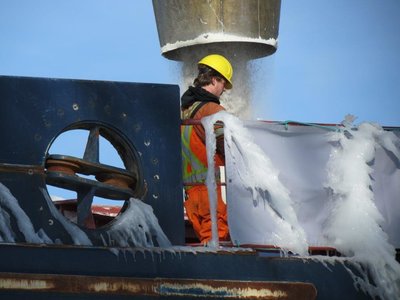 Crew member walks by the loading spout and appeared to be throwing ice melt on the deck as he walked along.